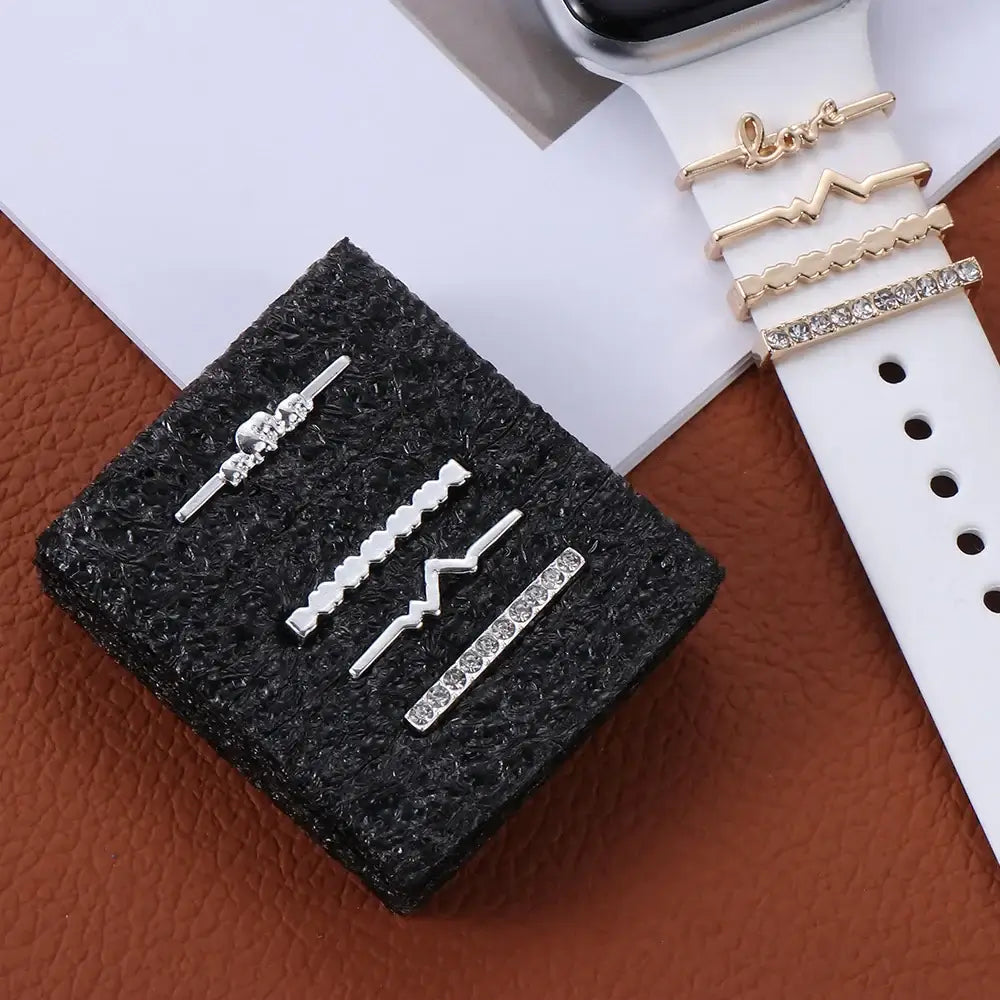Decorative metal charms for Apple bands displayed on a black cushion alongside a stylish smartwatch.