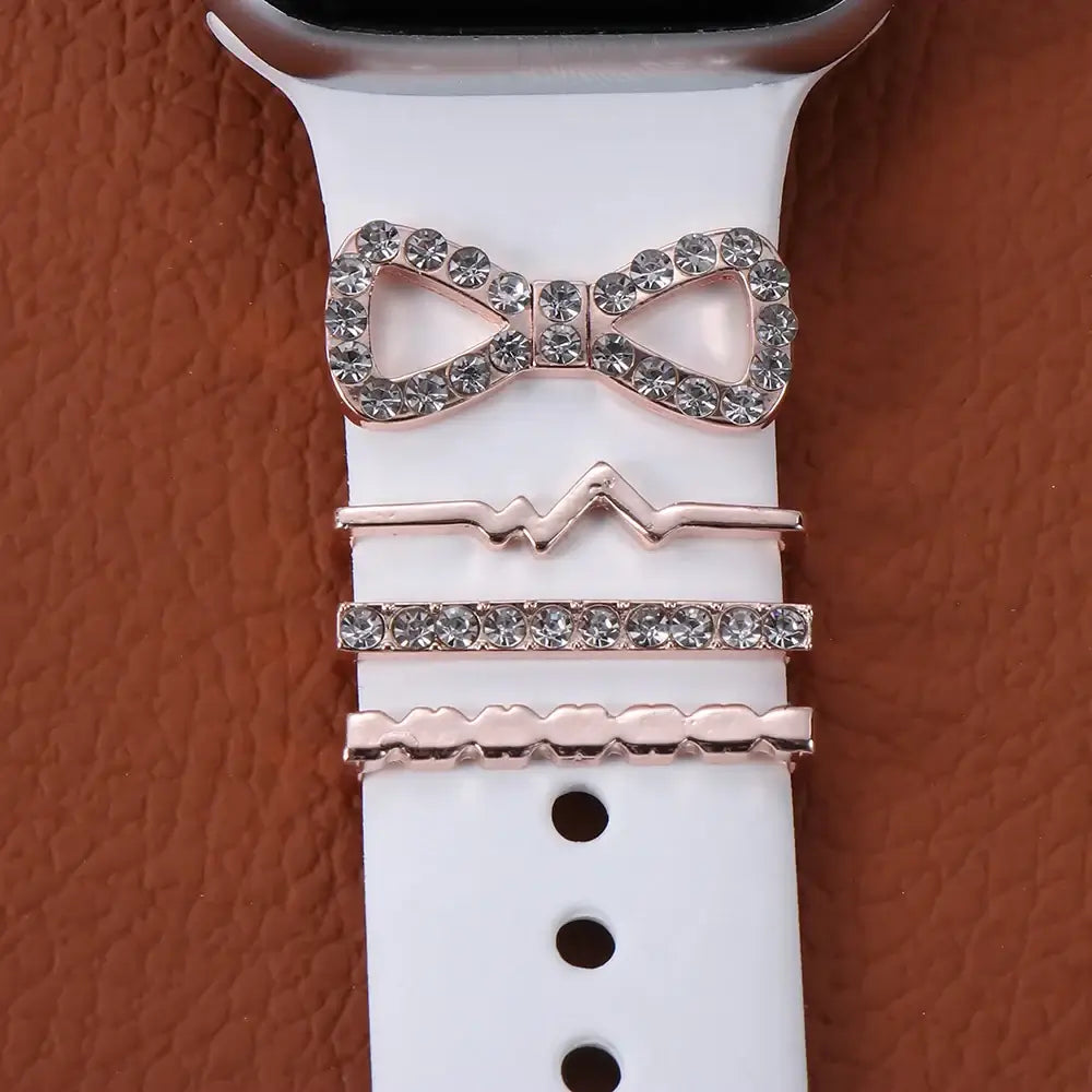 Decorative metal charms featuring a bow and sleek designs on a white Apple Watch band, enhancing your smartwatch style.