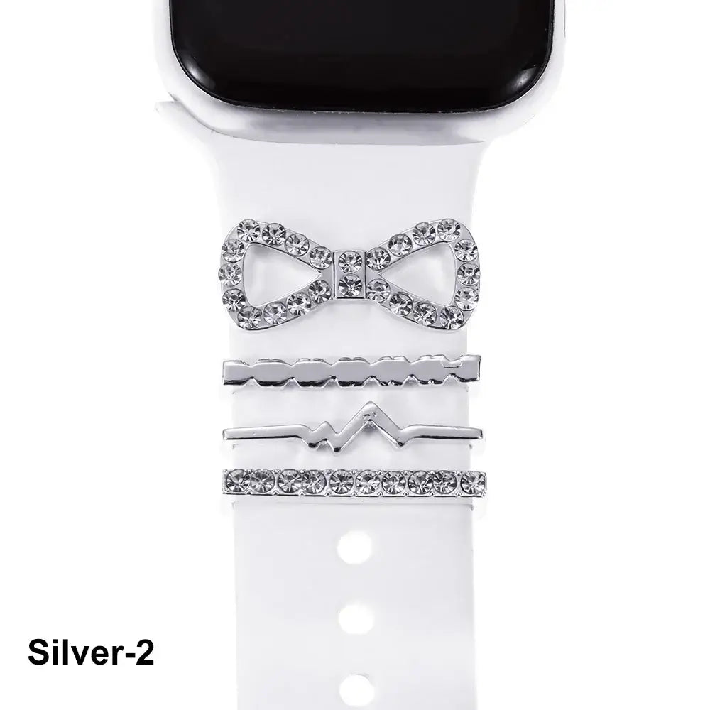 Decorative silver metal charms on white Apple Watch band, featuring a sparkling bow and stylish design elements.