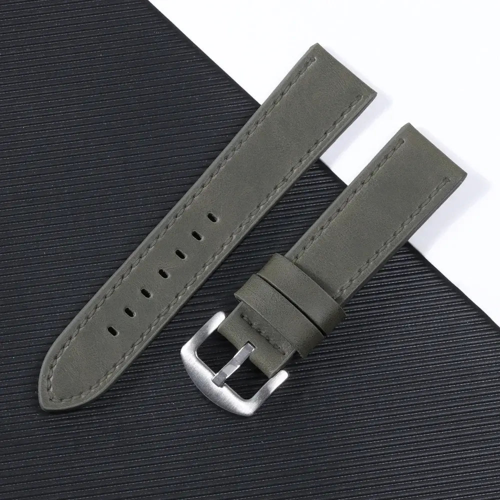 Olive green leather Suunto watch band with silver buckle on a textured black surface. Perfect for modern smartwatch styling.