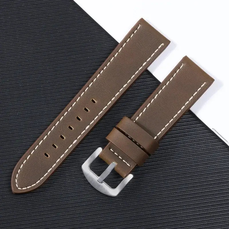 Brown leather Suunto watch band with white stitching and a silver buckle on a textured background.