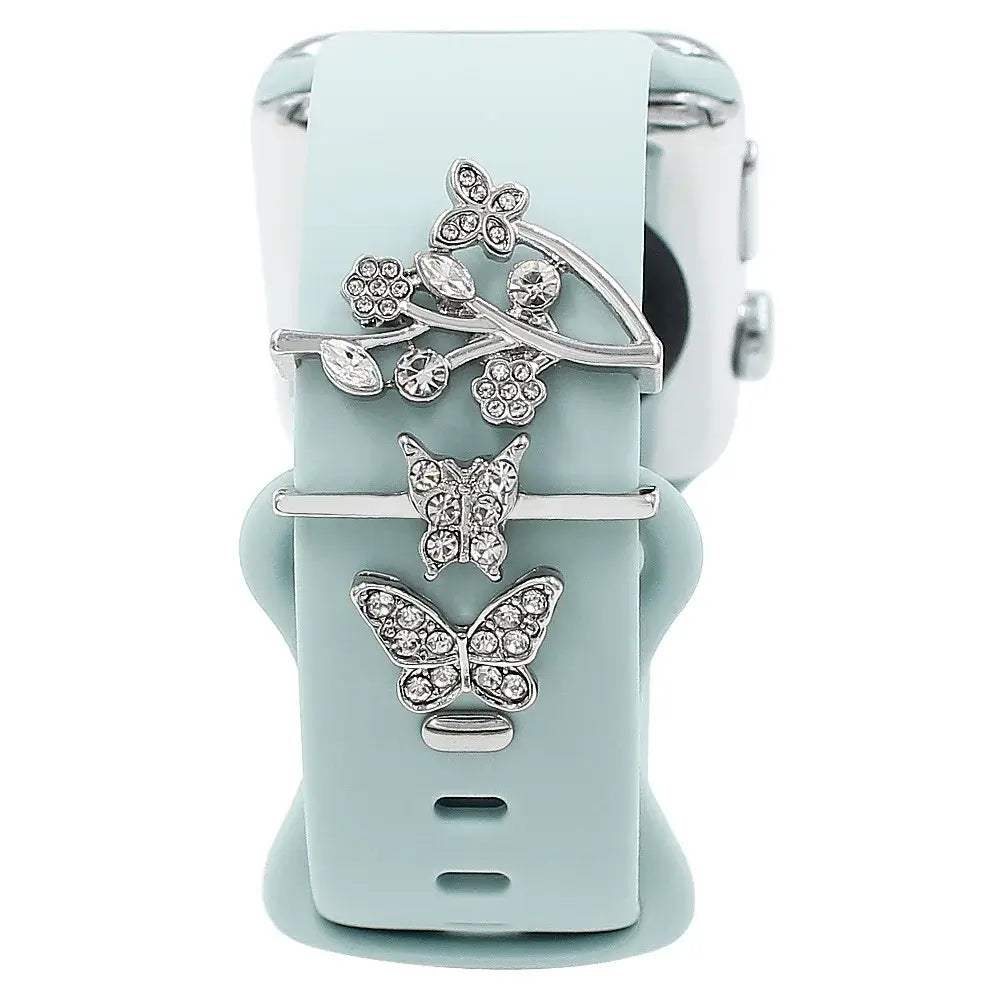 Decorative silver floral and butterfly charms on a mint green Apple Watch band, adding elegance and style.
