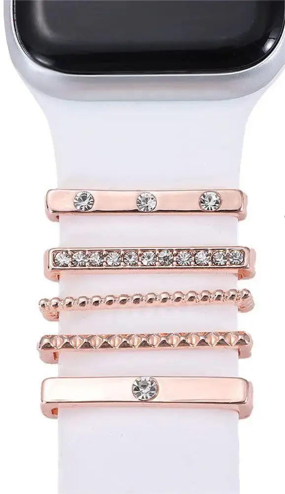 Decorative metal charms on a white Apple Watch band, featuring stylish rose gold accents and sparkling crystals.