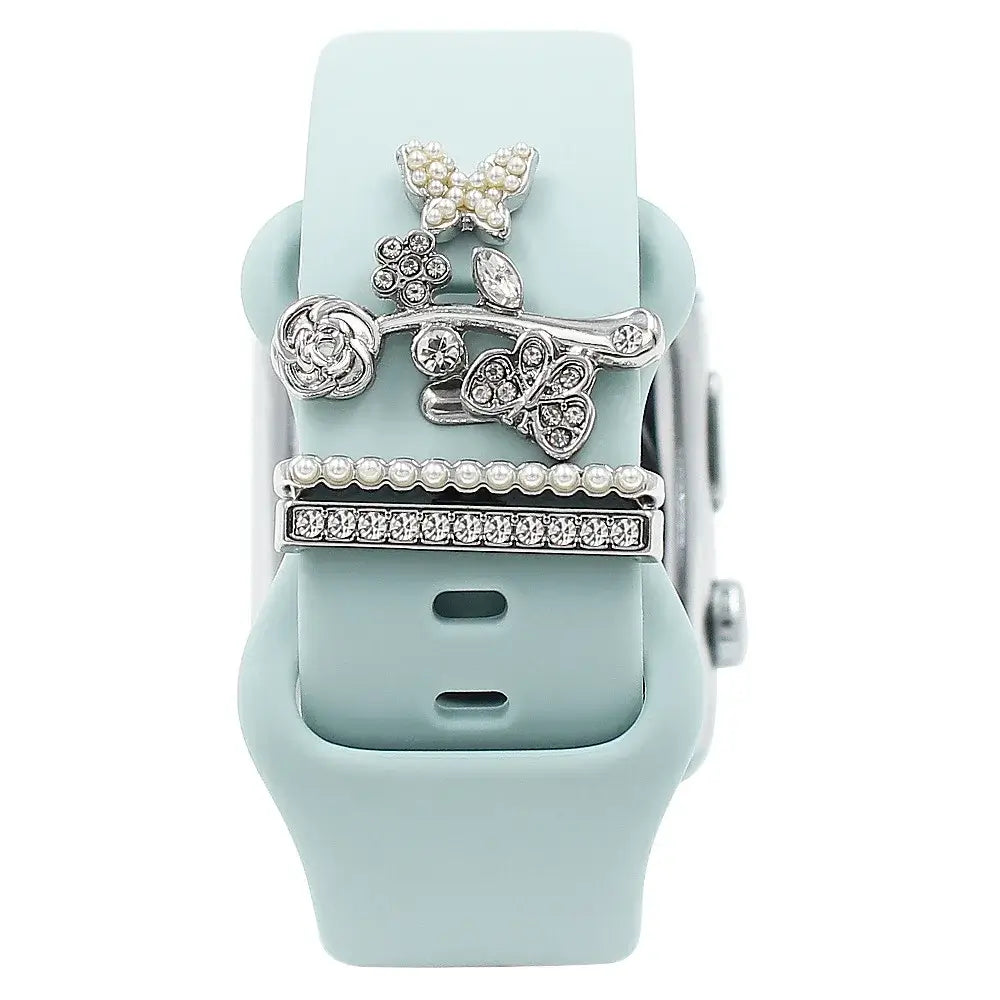 Decorative metal charms on a light blue Apple Watch band, featuring floral and butterfly designs for stylish elegance.