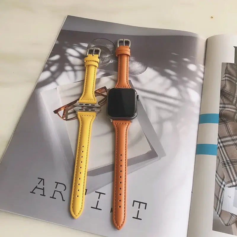 Slim leather Apple Watch straps in yellow and orange displayed on a magazine, showcasing stylish design and quality.