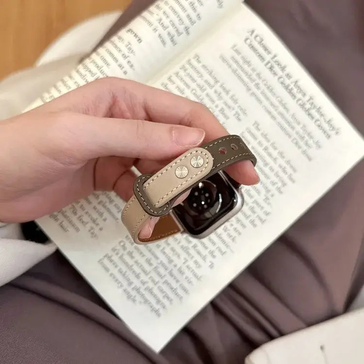 Elegant thin leather Apple Watch band held in hand, paired with an open book, showcasing style and sophistication.