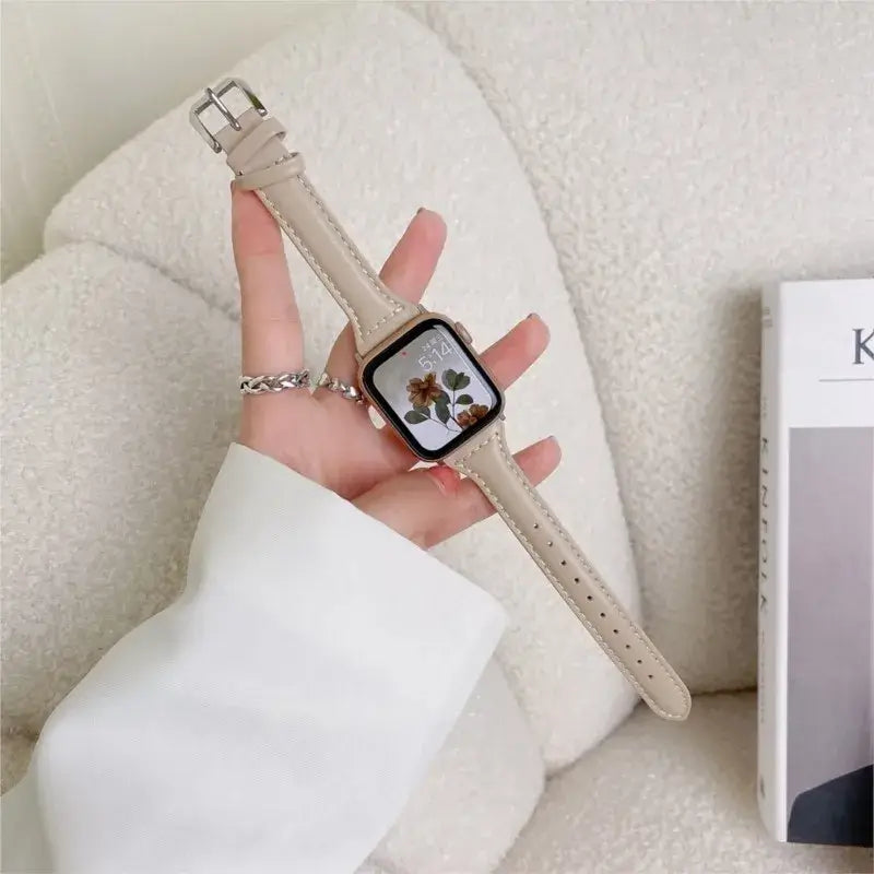 Slim beige leather strap for Apple Watch, showcasing a stylish and sophisticated look on a cozy surface.