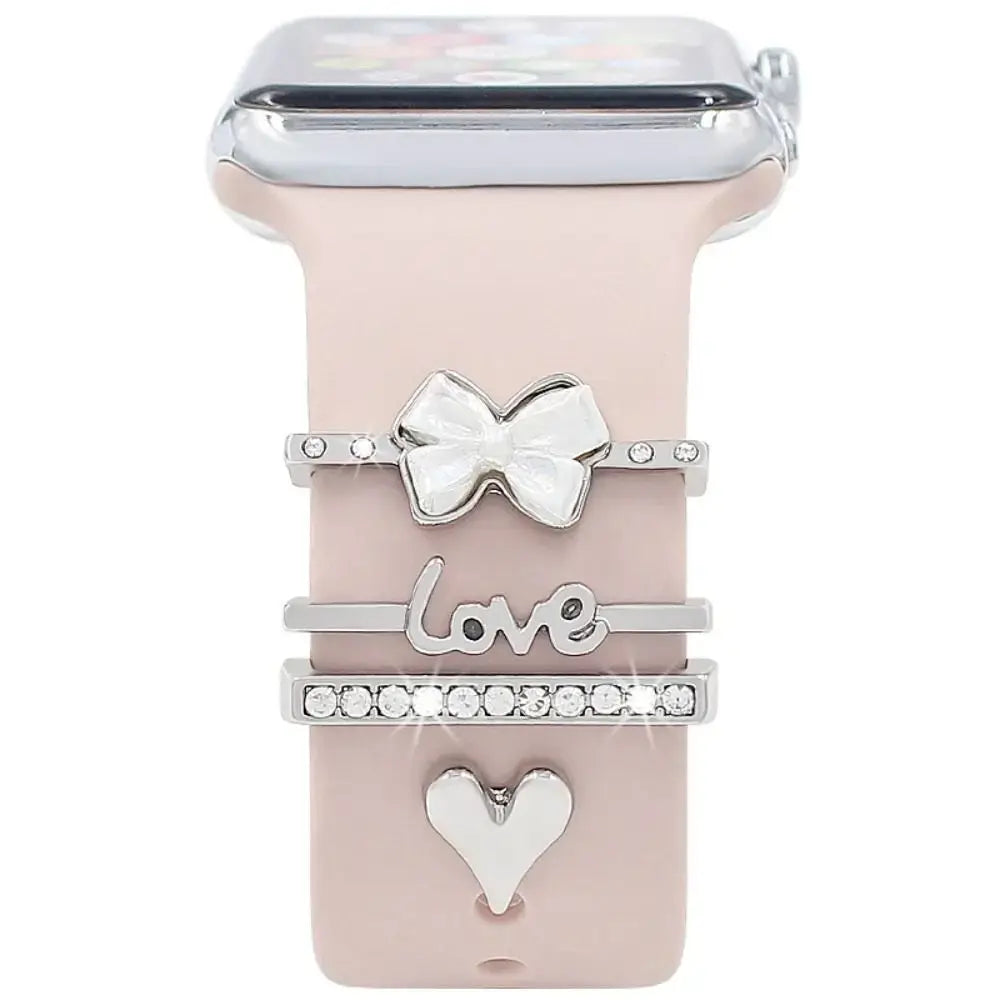 Decorative metal charms on a stylish Apple Watch band, featuring a bow, 'love' charm, and heart design for elegant flair.