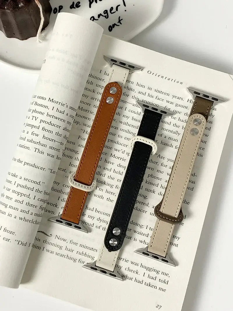 Thin leather Apple Watch bands in brown, black, and beige displayed on a book, showcasing style and elegance.