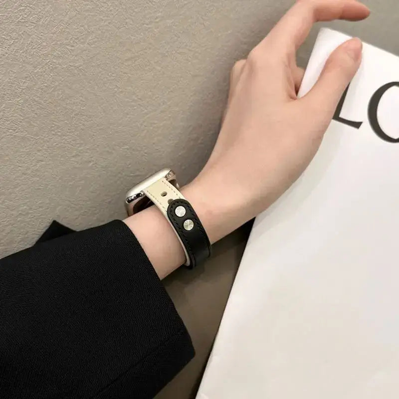 Hand wearing a sleek black leather Apple Watch band, showcasing style and elegance against a neutral background.