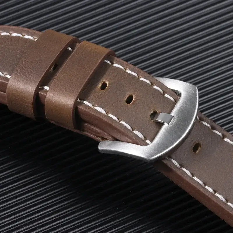Close-up of a brown leather Suunto watch band with silver buckle and white stitching on a textured black background.