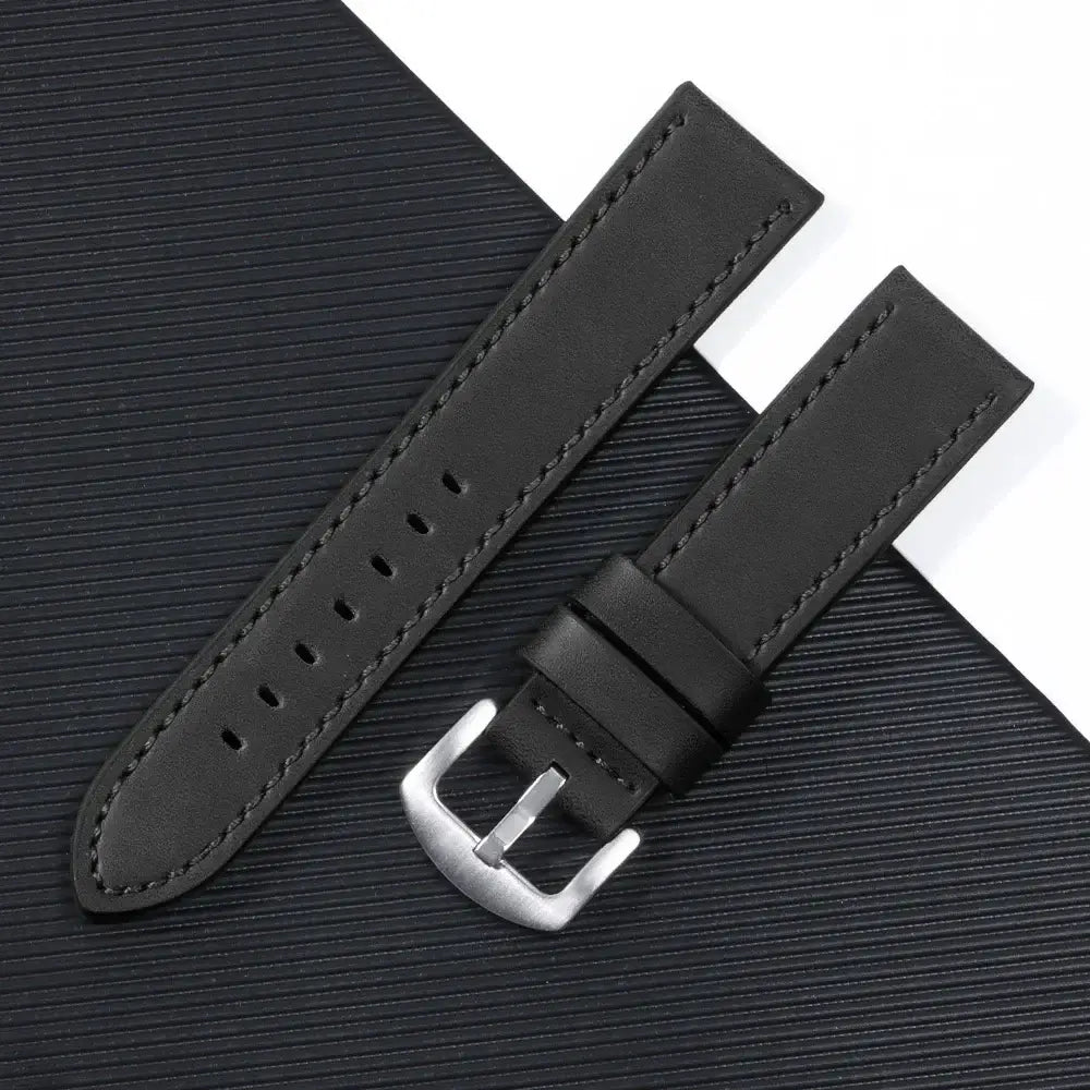 Black leather Suunto watch band with a silver buckle on a textured black background.
