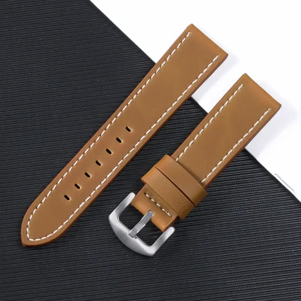 Suunto leather watch band in brown with silver buckle on a textured black background, showcasing sleek design and durability.