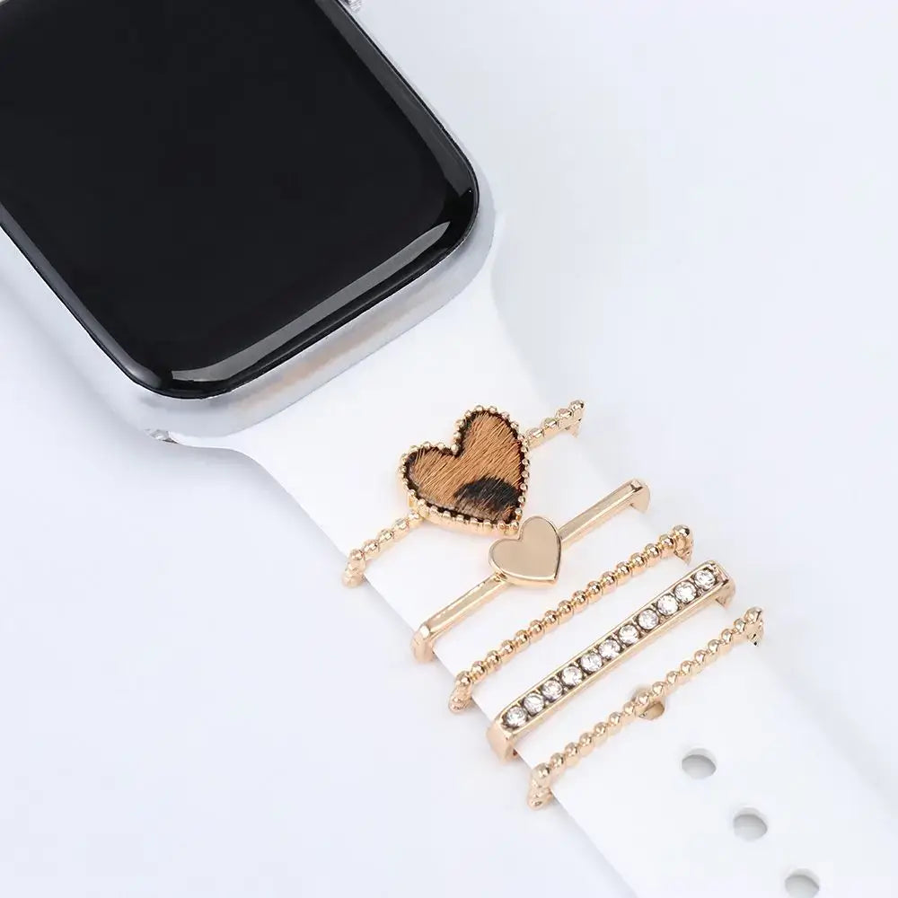 Decorative metal charms for Apple Watch bands in rose gold, showcasing stylish heart designs on a white strap.