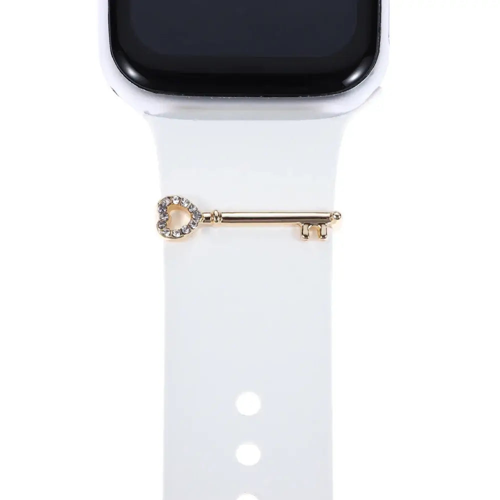 Decorative gold key charm with heart design on a white Apple Watch band for personalized style.