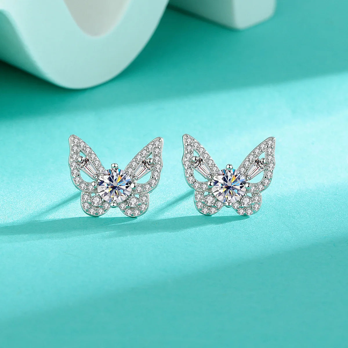 Butterfly Moissanite Stud Earrings in Sterling Silver — Pair on turquoise surface