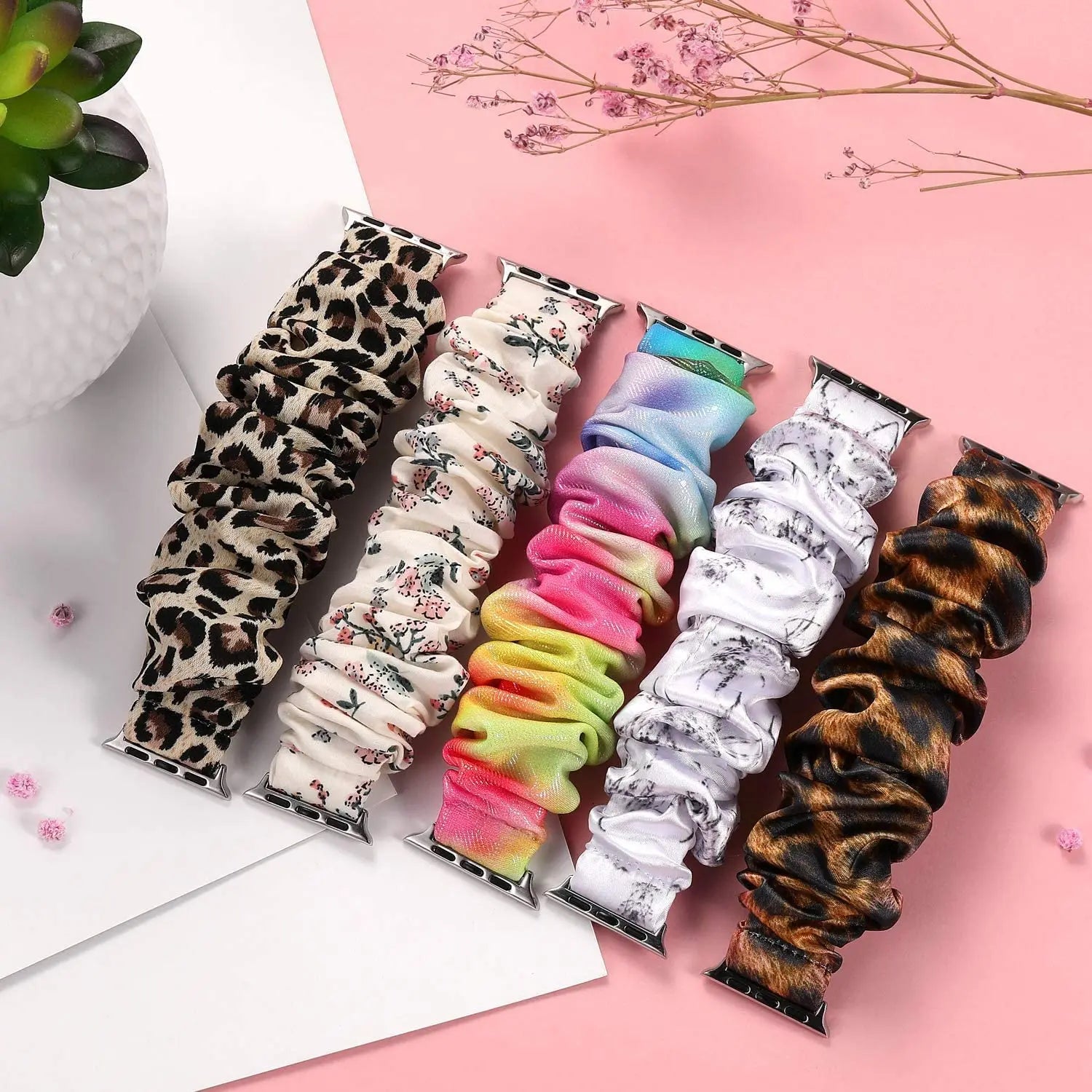 Colorful Apple Watch scrunchie straps in various patterns, including floral, leopard, and tie-dye, displayed stylishly.