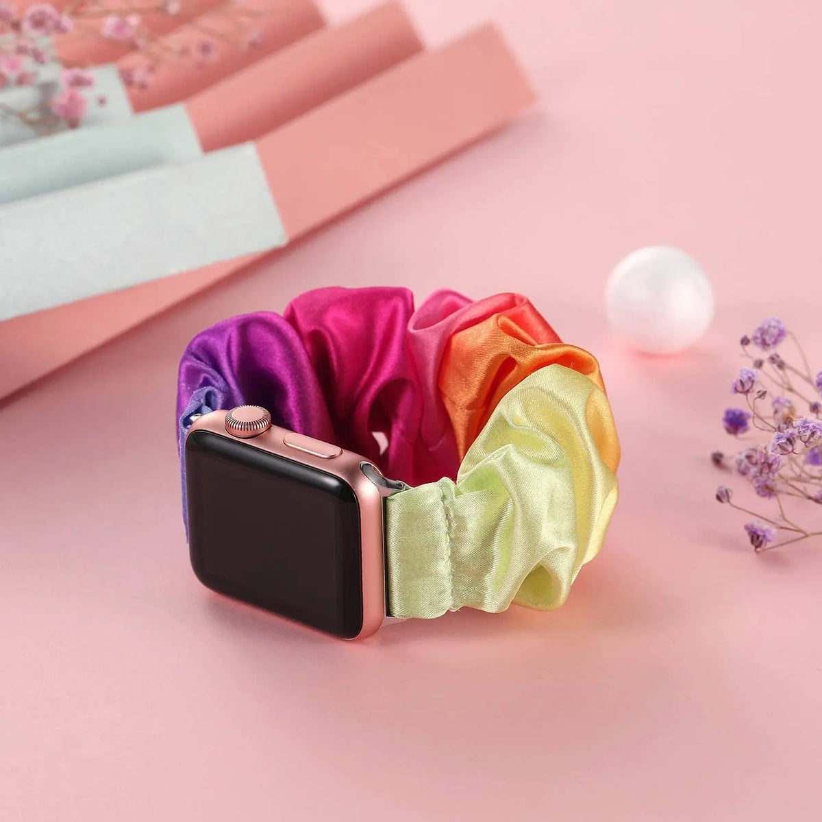 Rainbow scrunchie band displayed on pink surface for Apple Watch