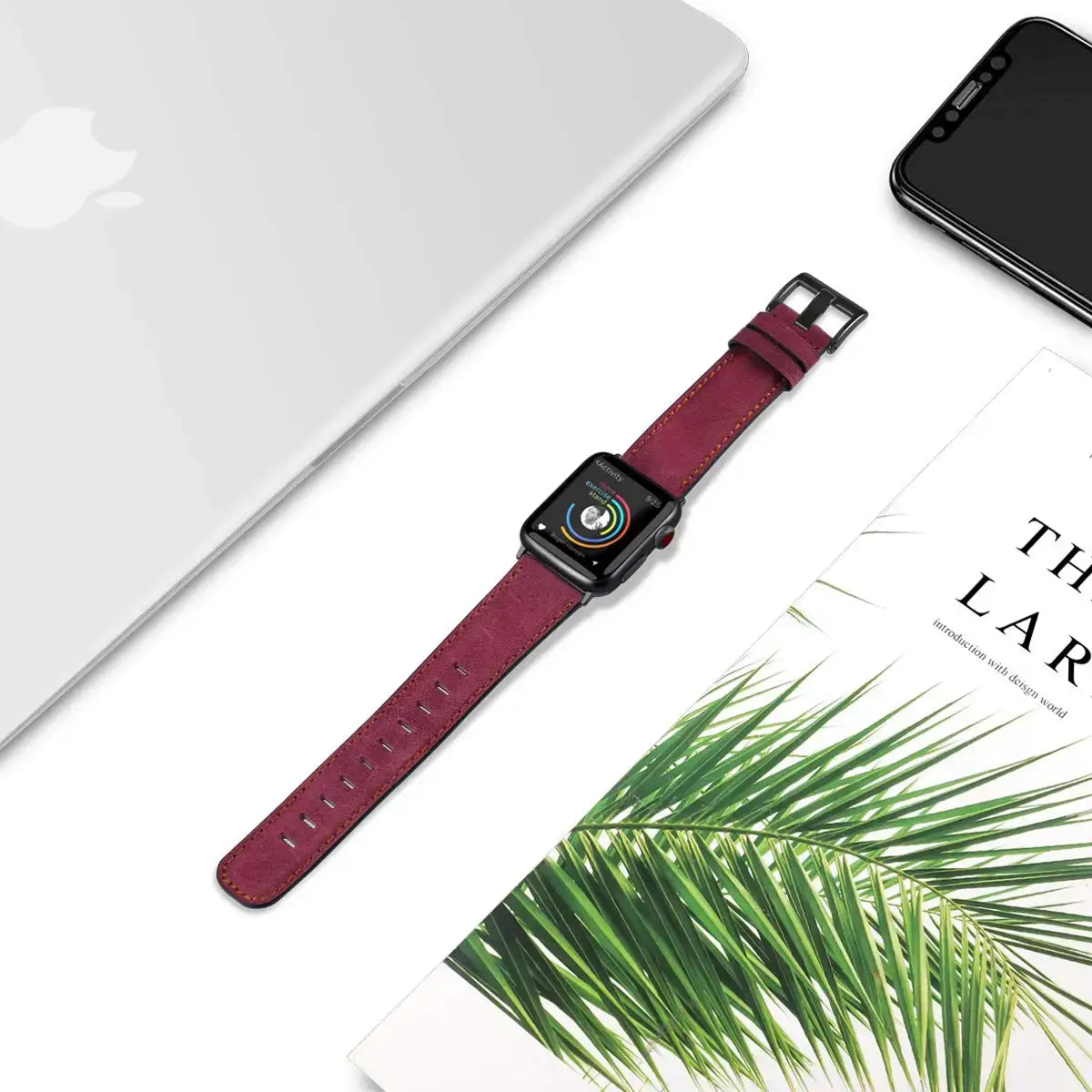 Burgundy leather Apple Watch strap laid flat beside desk accessories