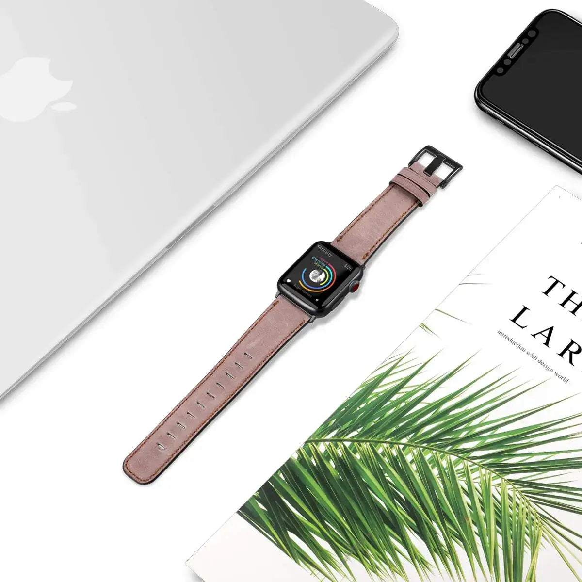 Dusty rose leather Apple Watch strap laid flat beside desk accessories