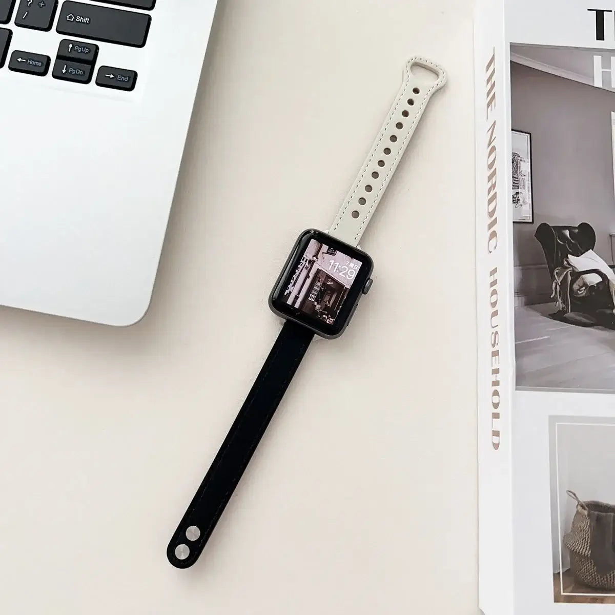 Thin leather Apple Watch band in black and white, showcasing style and elegance next to a MacBook and magazine.