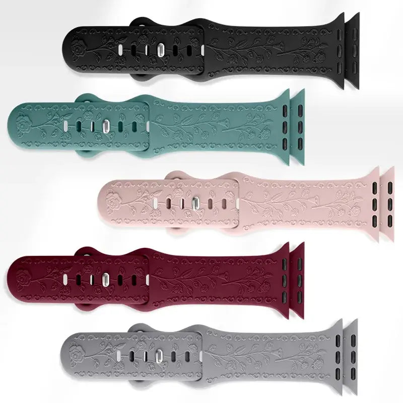 Five botanical engraved Apple Watch straps laid flat in different colors