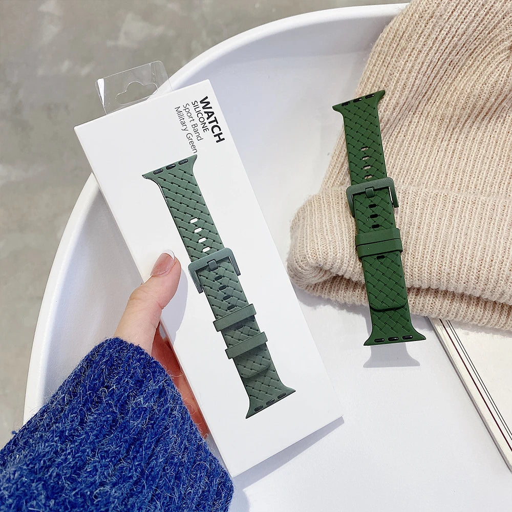 Apple Watch silicone strap in green, packaged with a cozy knit sweater in the background.