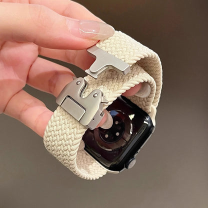 Close-up of a hand holding a beige Apple Watch with a braided nylon parachute strap and metal clasp.