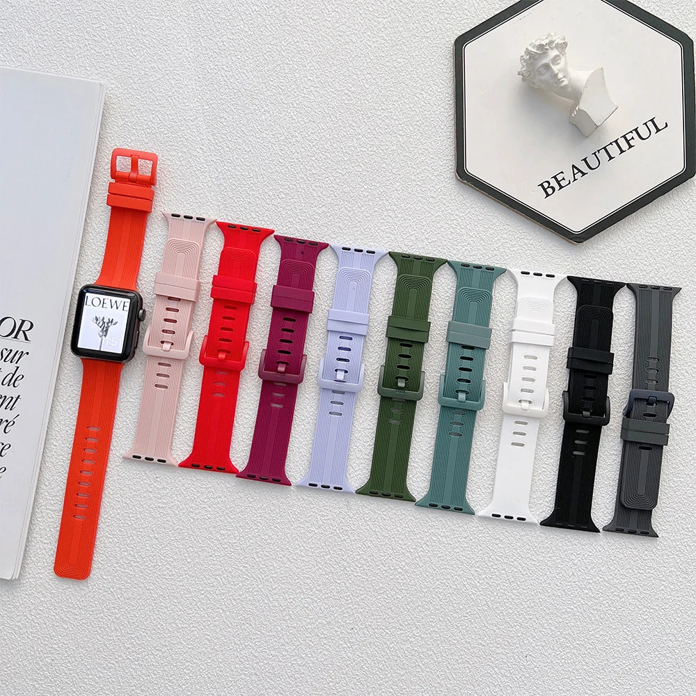 Various Apple Watch silicone straps in multiple colors displayed alongside a smartwatch on a textured surface.