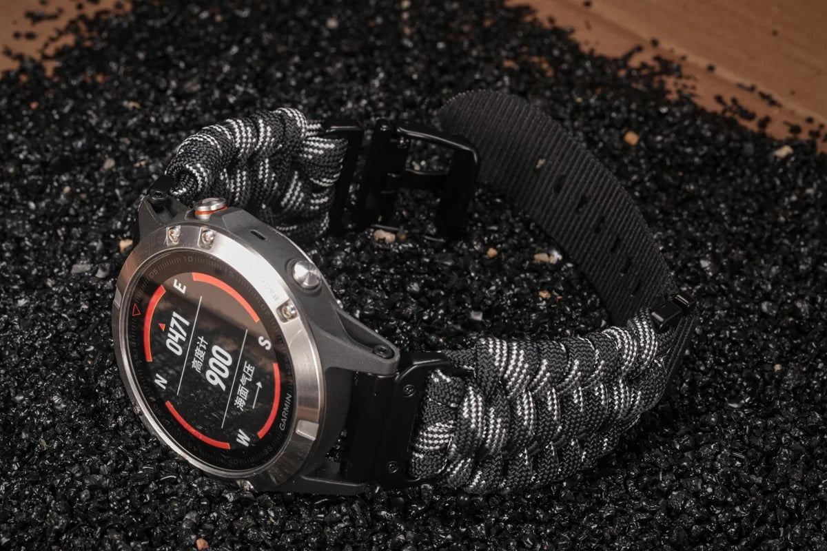 Garmin smartwatch with paracord band strap on black gravel surface, showcasing durable design for active lifestyles.