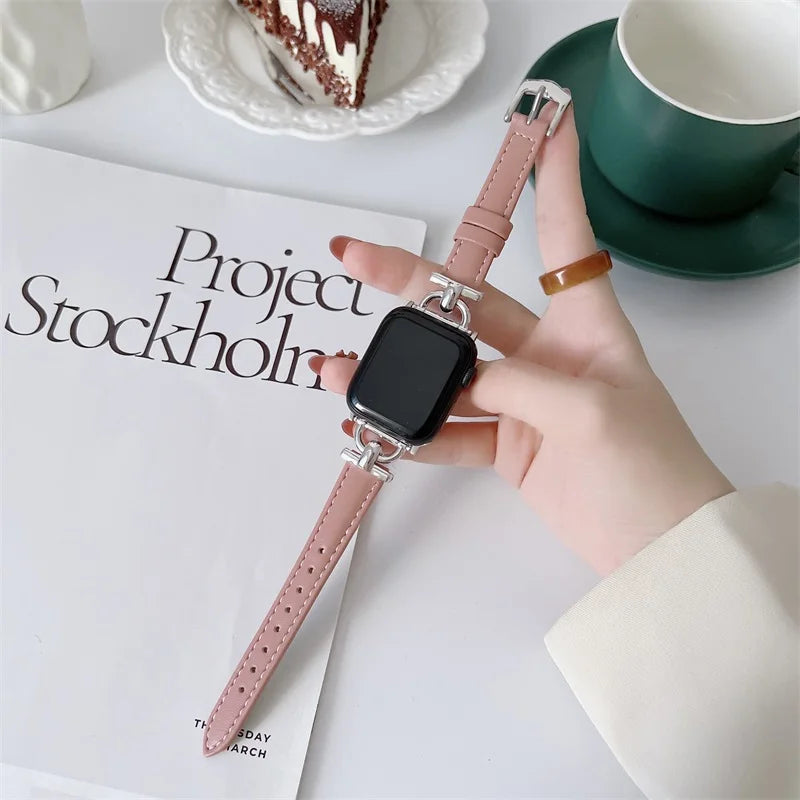Hand holding an Apple Watch with a pink genuine leather strap on a table with a coffee cup and a cake.