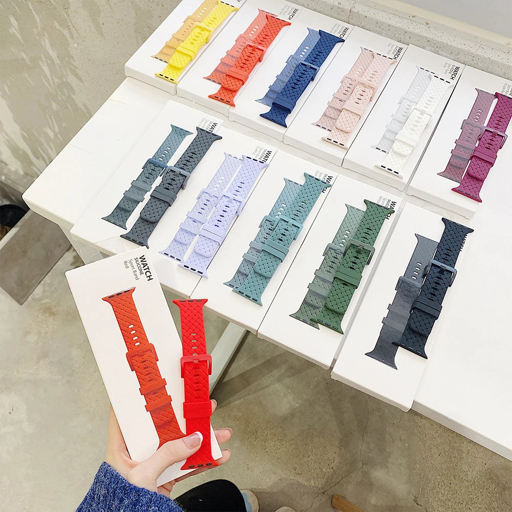 Variety of Apple Watch silicone straps in multiple colors displayed on a table with packaging.