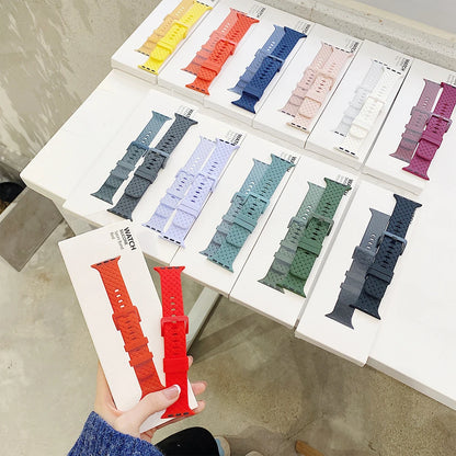 Variety of Apple Watch silicone straps in multiple colors displayed on a table with packaging.
