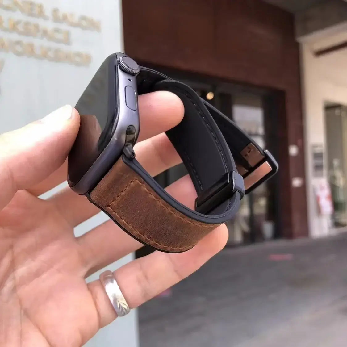 Brown leather Apple Watch band with magnetic clasp held in hand