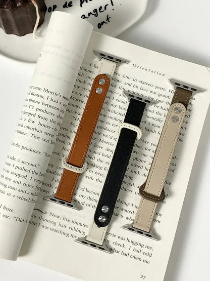 Thin leather Apple Watch bands in brown, black, and beige displayed on a book, showcasing style and elegance.