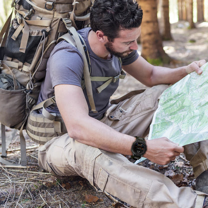 Man in the woods using a map while wearing a Garmin smartwatch with a tactical nylon strap.