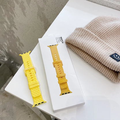 Bright yellow Apple Watch silicone strap displayed in packaging next to a beige knitted beanie.