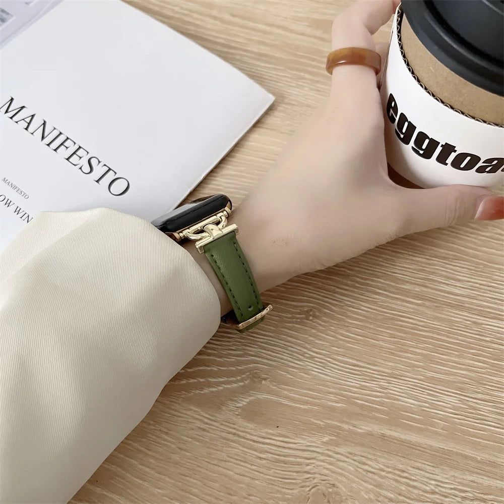 Stylish hand wearing an Apple Watch with a green genuine leather strap, holding a coffee cup on a wooden table.