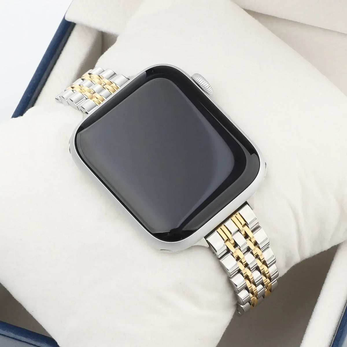 Silver and gold multi-link Apple Watch bracelet resting on fabric