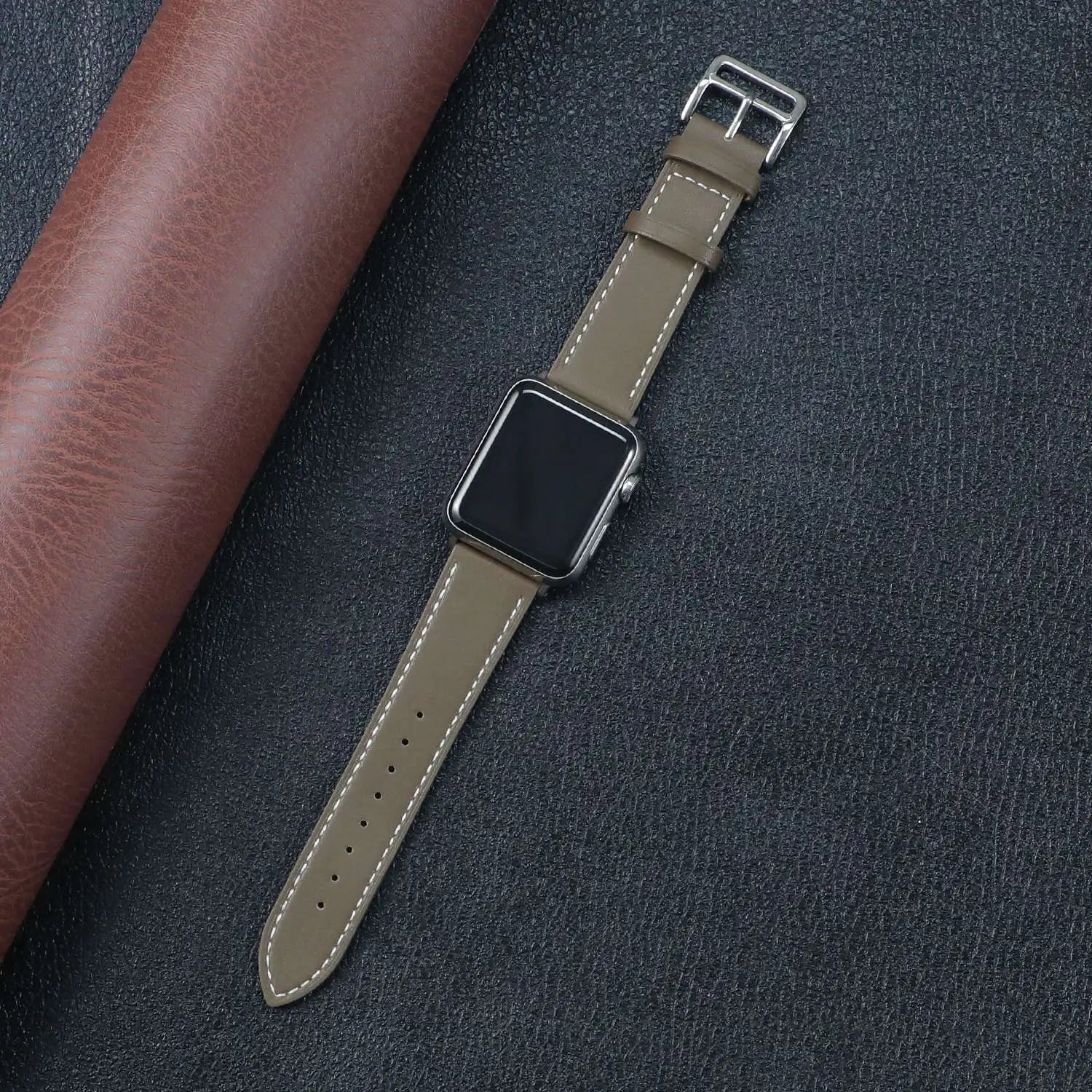 Apple Watch fabric band in olive green with metal buckle clasp on a textured black background.