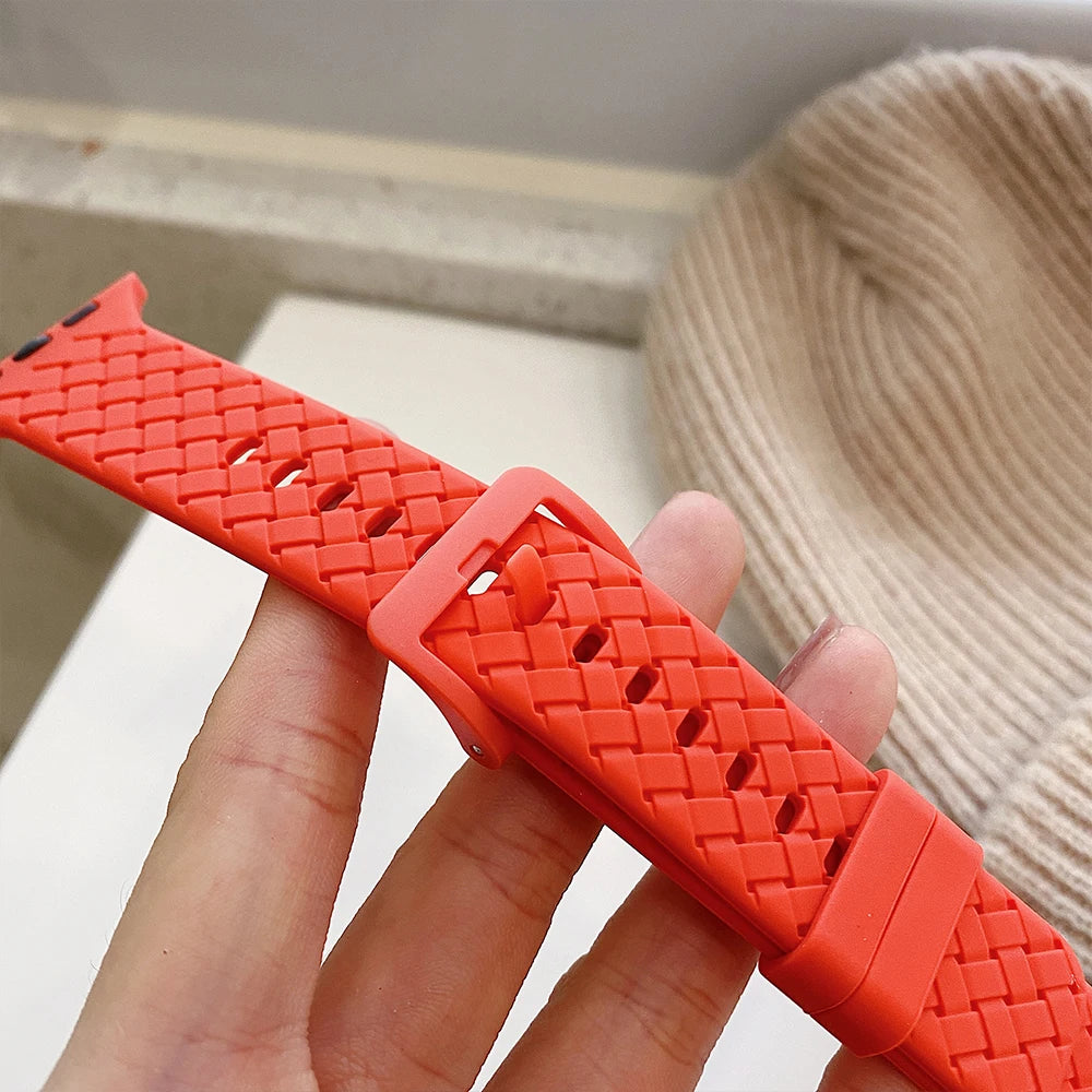 Close-up of an orange silicone strap for Apple Watch, showcasing its braided design and adjustable buckle.