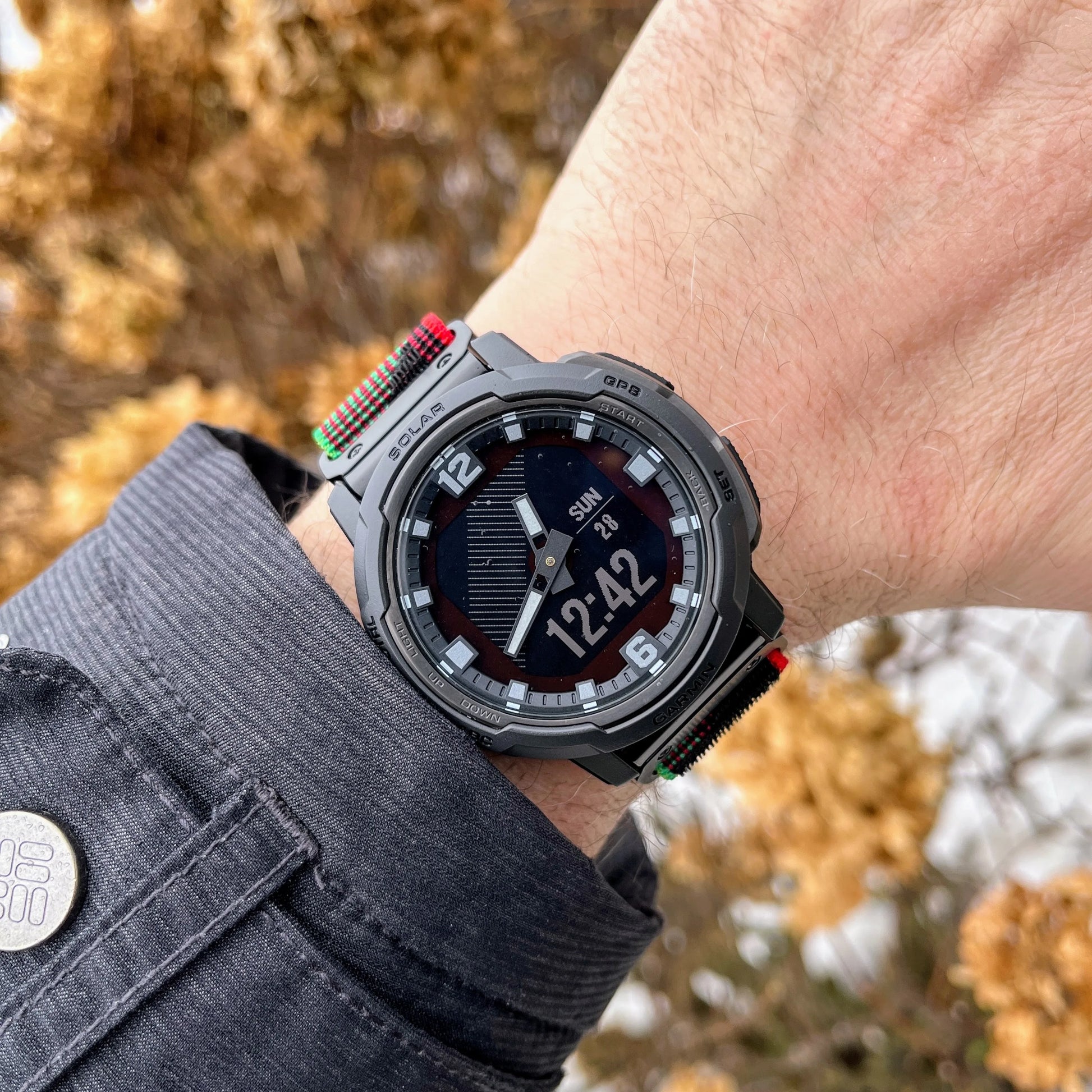 Garmin smartwatch on a wrist with a rugged woven nylon band, showcasing time display against a natural background.