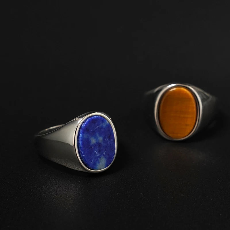 Oval tiger's eye titanium steel ring beside a blue stone version