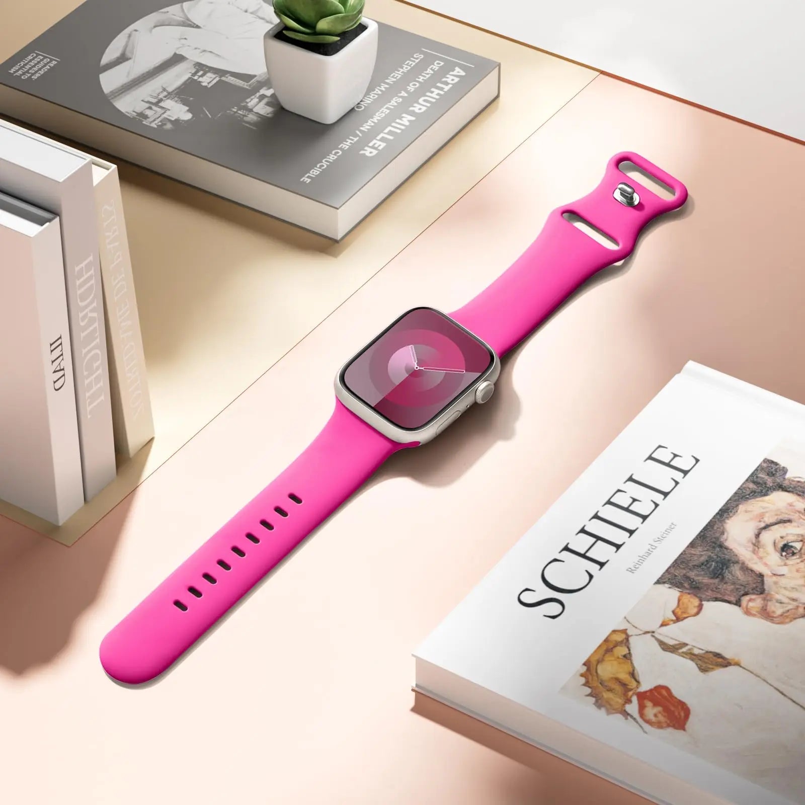 Apple Watch with a pink silicone strap on a stylish table with magazines and a plant.