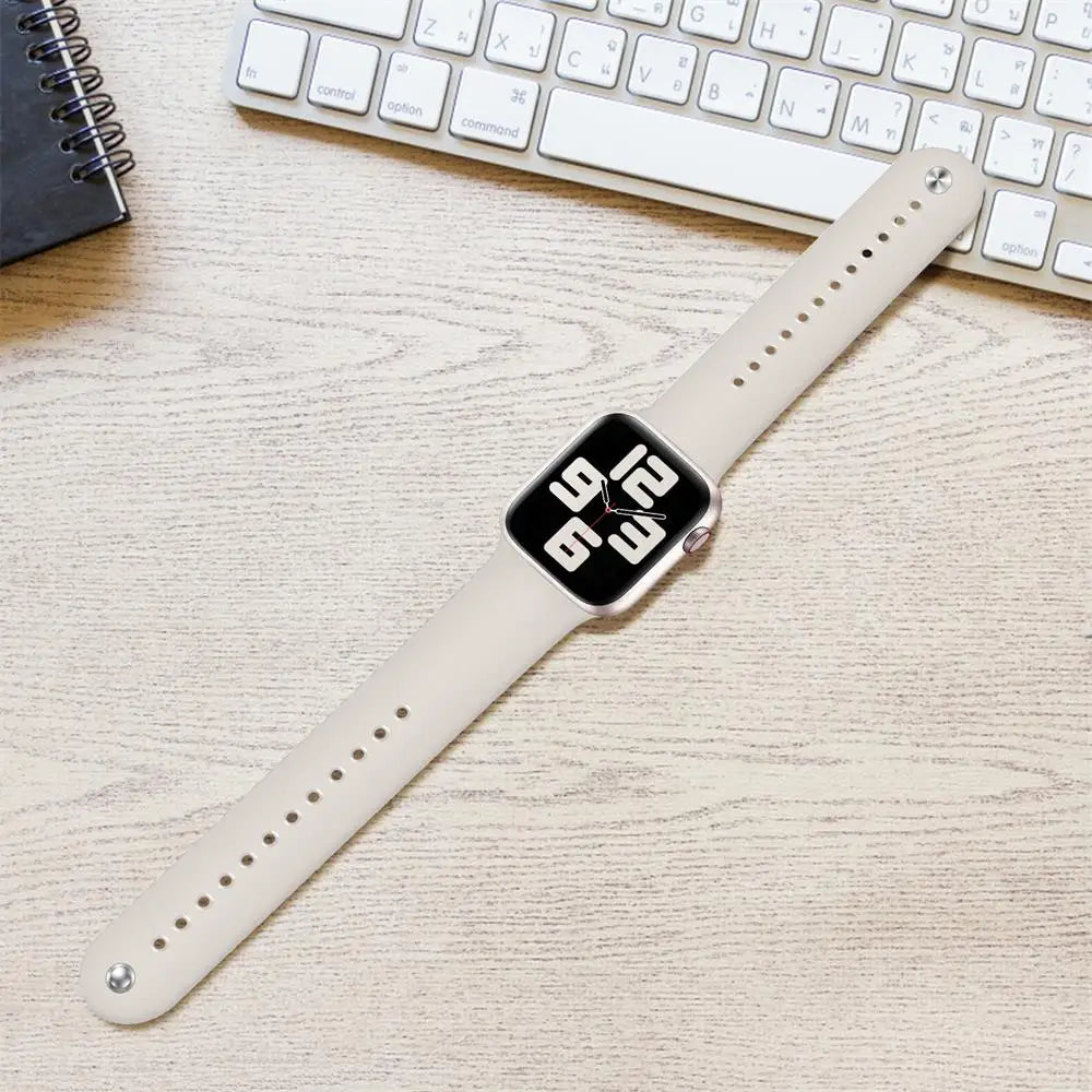 Apple Watch Silicone Strap in soft beige color on a wooden desk with a keyboard, showcasing its comfortable and waterproof design.